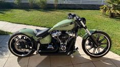 a green motorcycle parked on top of a sidewalk next to a lush green field with palm trees