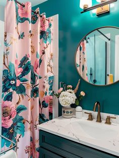 a bathroom decorated in teal and pink with flowers on the shower curtain next to the sink