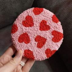 a hand holding a red and white crocheted brooch with hearts on it