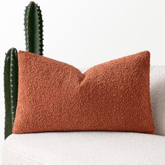 an orange pillow sitting on top of a white couch next to a green cactus plant