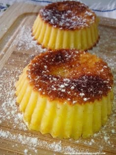 two desserts sitting on top of a wooden cutting board covered in powdered sugar