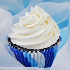 a cupcake with white frosting sitting on top of blue paper