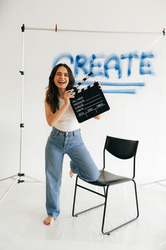 a woman standing in front of a chair holding a clap board