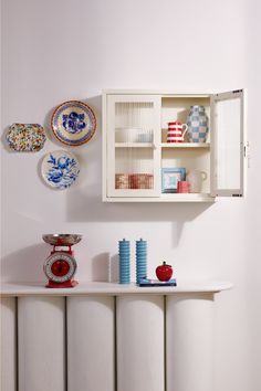 a white shelf with plates and vases on it next to a radiator