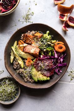 a bowl filled with lots of food next to sliced oranges and other fruits on top of a table