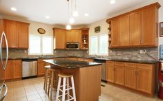 a large kitchen with wooden cabinets and black counter tops, stainless steel appliances and an island in the middle