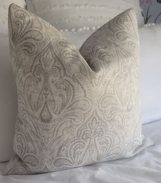 a close up of a pillow on a bed with white sheets and pillows in the background