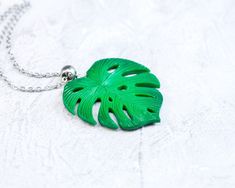 a necklace with a green leaf on it sitting on top of a white tablecloth