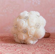 a bridal bouquet sitting on top of a pink table cloth covered in white flowers