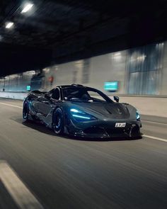 a black sports car driving down the road at night time with lights on it's hood