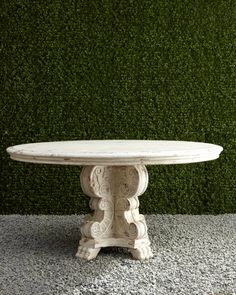 a white table sitting on top of a stone floor next to a green grass covered wall