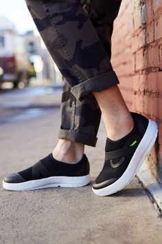 a person standing next to a brick wall wearing black and white slip ons with green accents