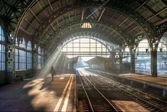 the sun shines through the windows in an empty train station as people walk on the platform