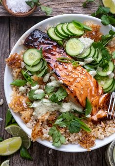 a white plate topped with rice, cucumbers and salmon