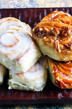 some cinnamon rolls are sitting on a red plate with white icing and pecans