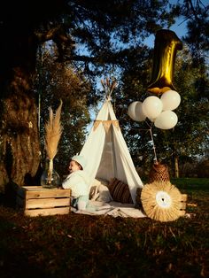 a teepee tent and some balloons in the grass with a person laying on it