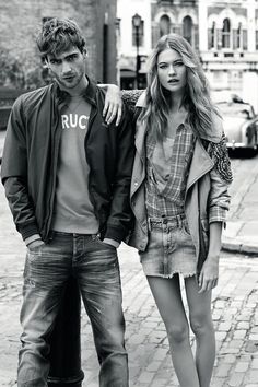 a man and woman standing next to each other on a brick road with cars in the background