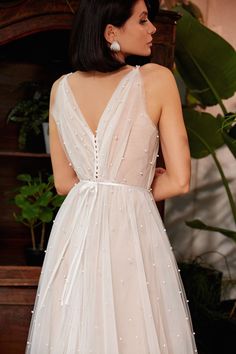 the back of a woman wearing a white dress with beaded detailing and pearls on it