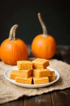 several pieces of pumpkin cake on a white plate next to two small orange pumpkins