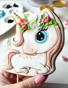 a close up of a person holding a cookie shaped like a unicorn with flowers on its head