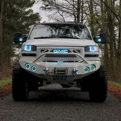 a white truck with lights on driving down a road next to trees in the woods