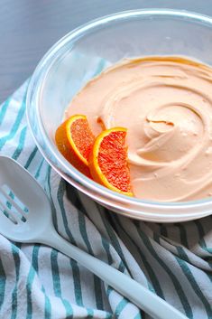 a bowl filled with oranges and cream on top of a striped towel next to spoons