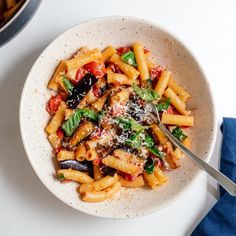 a white bowl filled with pasta and vegetables on top of a table next to a blue napkin