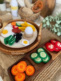 an assortment of crocheted food items on a tray next to a basket with flowers