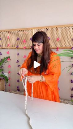 a woman in an orange dress is working on something with white yarn and scissors at a table