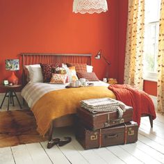 a bedroom with orange walls and white flooring, luggage on the floor in front of the bed