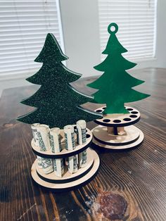 two wooden christmas trees sitting on top of a table next to each other with money in front of them