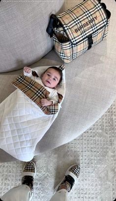 a baby wrapped in a blanket sitting on top of a couch next to a duffel bag