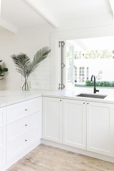 a kitchen with white cabinets and wood flooring next to an open window that looks out onto the backyard