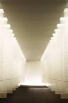 an empty hallway with white columns and light at the end