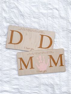 two wooden magnets with hand prints on them sitting on a white sheeted surface