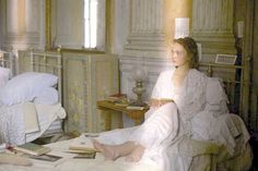 a woman sitting on top of a bed in a bedroom next to a table with books