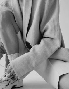 a woman sitting on the ground with her legs crossed wearing sneakers and a blazer