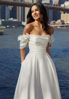 a beautiful woman in a white dress standing by the water with her hands on her hips