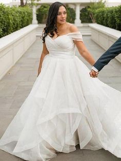 a bride and groom hold hands as they walk down the sidewalk