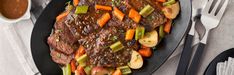 a steak with carrots, celery and potatoes on a black plate next to silverware