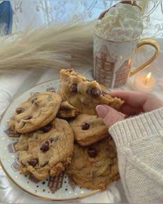 chocolate chip cookies on a plate next to a coffee cup and teacup with a lit candle