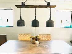 a dining room table with three lights hanging from it's ceiling and two vases on each side