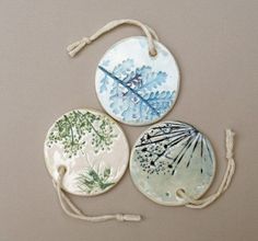 three ceramic coasters with designs on them are hanging from twine cords and string