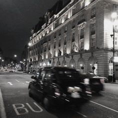 a black and white photo of cars driving down the street in front of a building