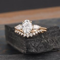 an engagement ring with three pear shaped diamonds on top of a black stone slab in front of a wooden background