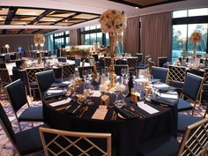 a banquet room set up with black table cloths and gold chairs, tall centerpieces