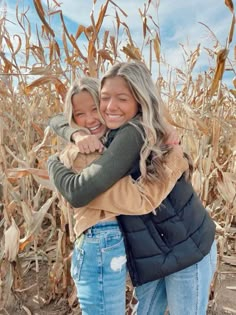 two women hugging each other in front of a corn field