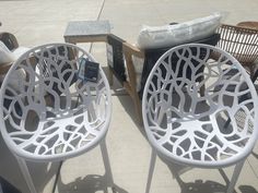 two white chairs sitting next to each other on top of a cement floor covered ground