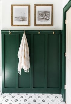 two framed pictures hang on the wall next to a green coat rack in a bathroom