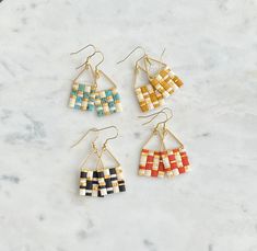 four pairs of multicolored earrings sitting on top of a marble counter with gold ear wires